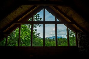 Une pièce dotée d’une grande fenêtre, avec une charpente en bois et une vue sur un paysage boisé.