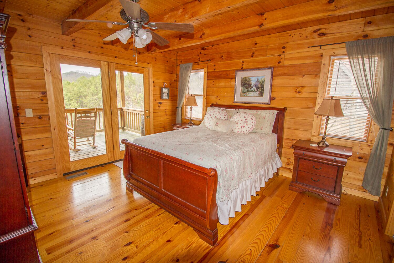 A wooden cabin bedroom with a bed, a nightstand, a ceiling fan, and a balcony door.