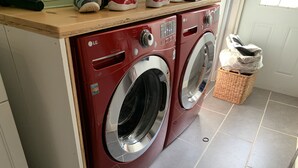 A red LG front-loading washing machine with a control panel and a stainless steel door, placed on a tiled floor with a wooden countertop above. - Private home minutes from Siesta Key and Downtown Sarasota. (Sarasota)