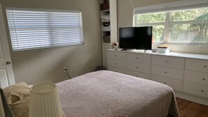 A bedroom with a bed, a TV on a dresser, a window with blinds, and a shelf with items. - Private home minutes from Siesta Key and Downtown Sarasota. (Sarasota)