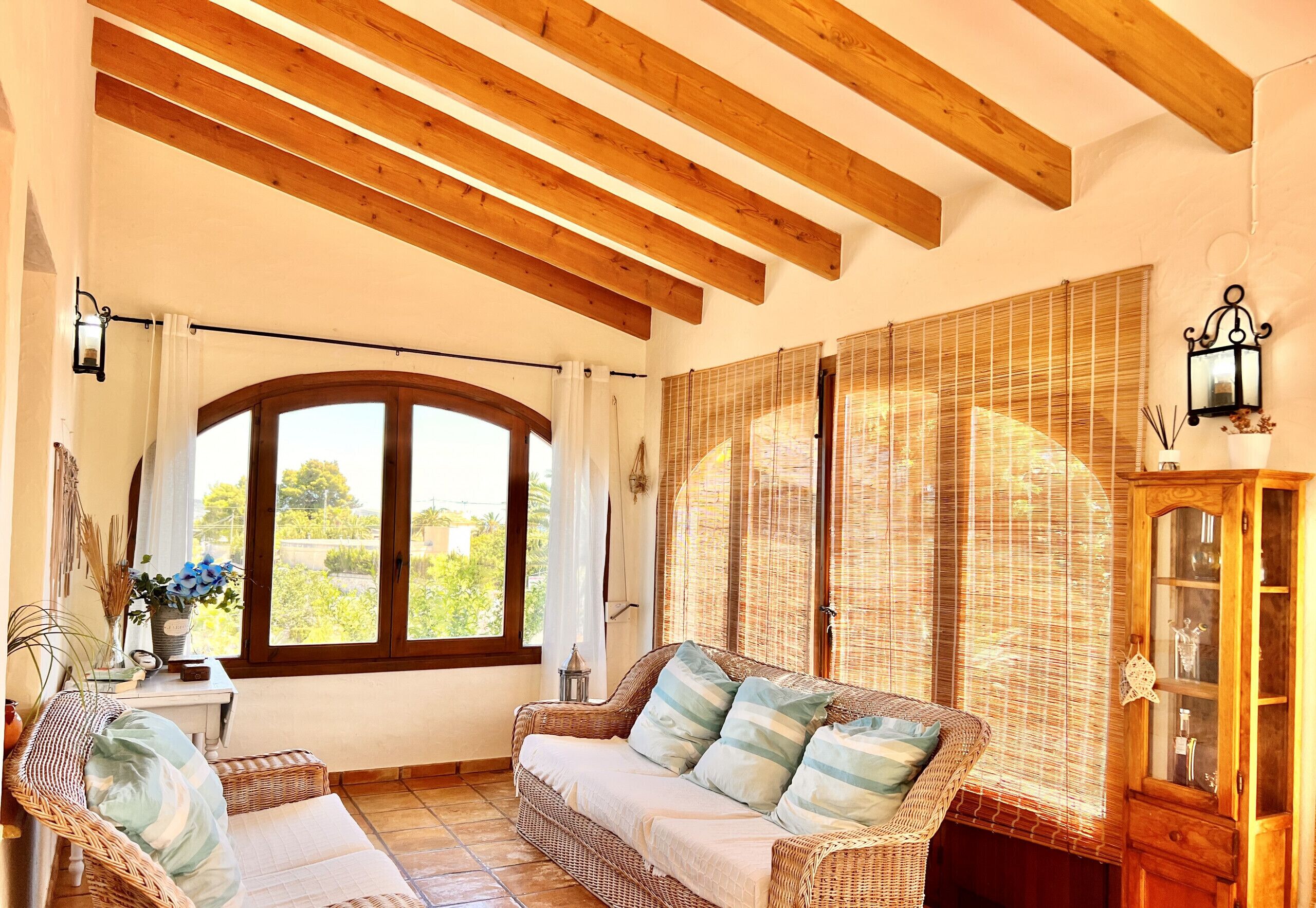 A cozy room with a wicker sofa, a wooden cabinet, and a large window with blinds.