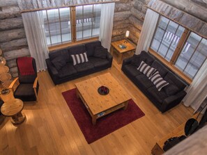 A log cabin interior with two dark sofas, a wooden coffee table, and a red rug.