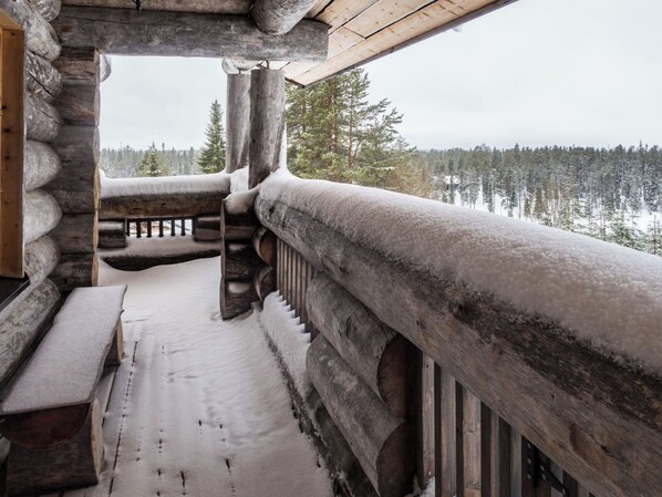 A log cabin with a snow-covered deck and a view of a forest.