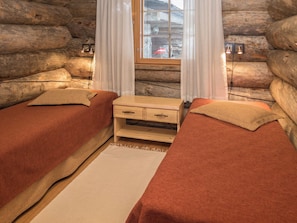 Een blokhutkamer met twee bedden, een klein houten nachtkastje en een raam met gordijnen.