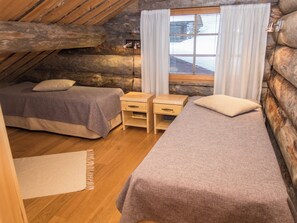 Une chambre confortable dans un chalet en rondins, avec deux lits, un petit bureau et une fenêtre avec des rideaux.