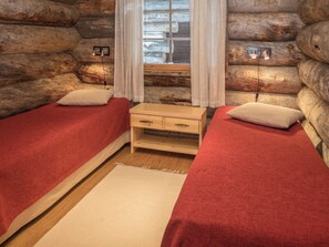Een kamer met een blokhut, twee bedden, een houten nachtkastje en een raam met gordijnen.