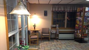 A cozy room with a round wooden table, two chairs, a small table with a potted plant, a window with blinds, a radiator, and a magazine rack. - Spinning Wheel Inn Branson (Branson)