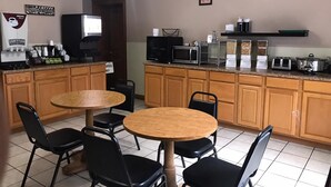 A small, clean cafe with wooden cabinets, a coffee machine, a microwave, and a TV. There are four black chairs around a wooden table. - Spinning Wheel Inn Branson (Branson)