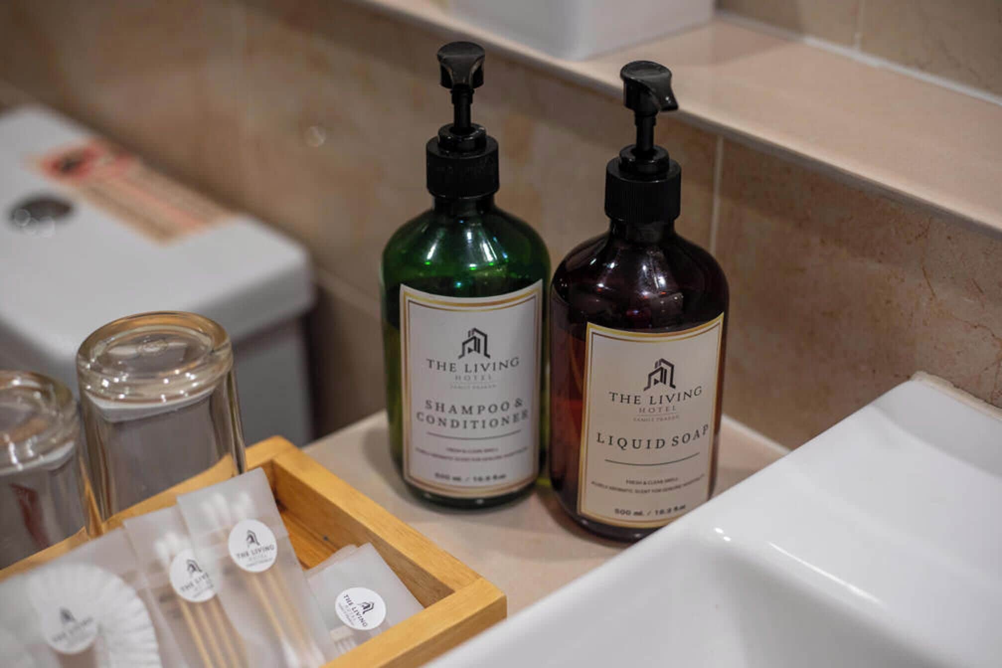 Un comptoir de salle de bain avec deux bouteilles de shampoing et d’après-shampoing, un verre d’eau et un plateau en bois contenant des articles de toilette.