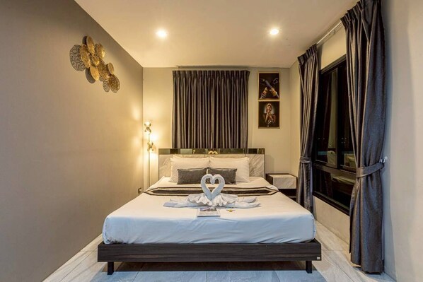 Une chambre d’hôtel avec un lit, une table de chevet, un luminaire fixé au mur et une fenêtre avec des rideaux.
