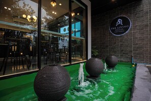 L’extérieur d’un hôtel avec une piscine artificielle verte, de grands vases décoratifs et une enseigne indiquant « The Living Hotel ».