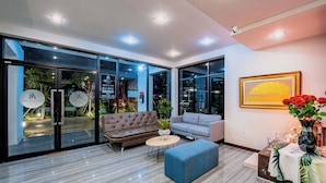 A modern interior with a sofa, a blue ottoman, and a small table. - The Living Hotel SamutPrakan (Bang Bo)