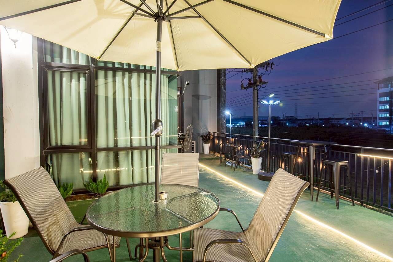 An outdoor balcony with a glass table, chairs, and a large umbrella.