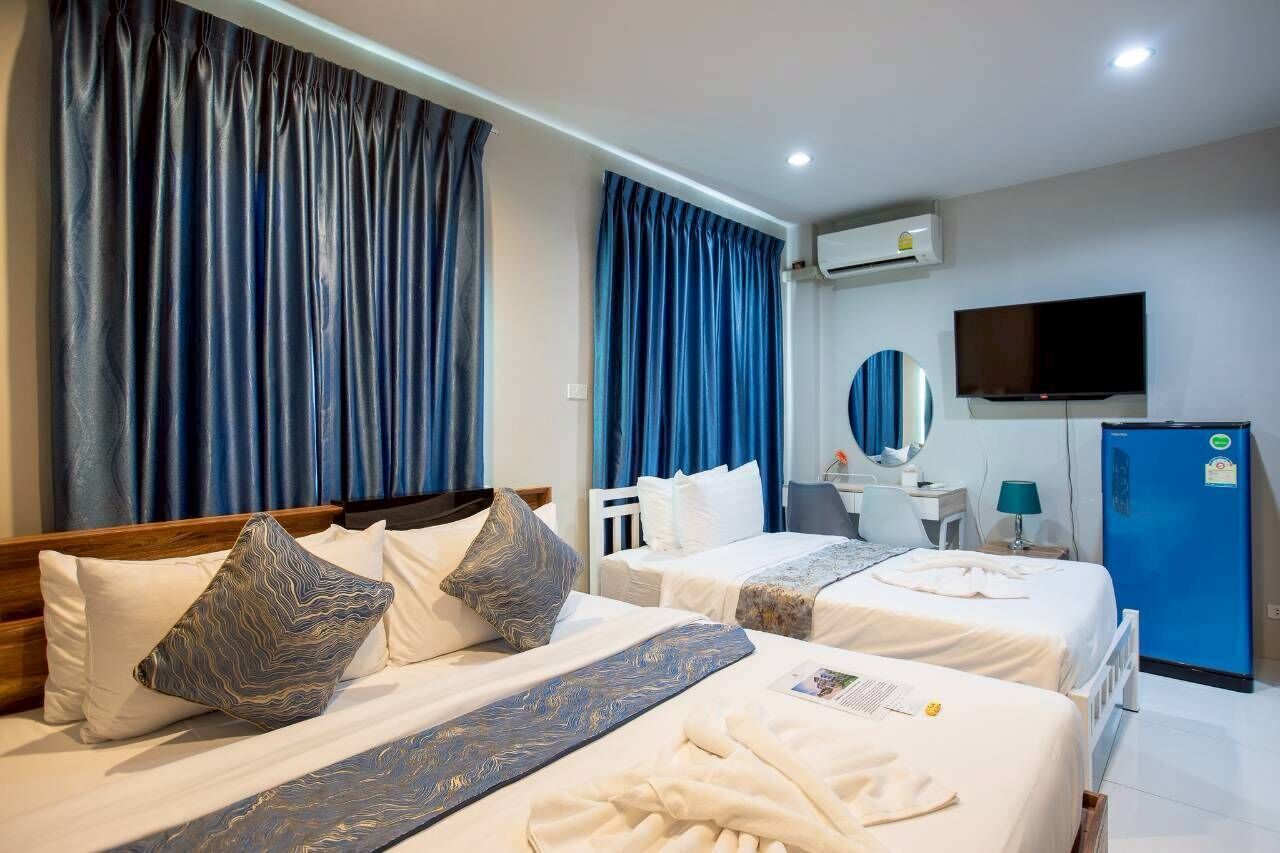 Habitación de hotel con dos camas, un televisor, un refrigerador azul y un equipo de aire acondicionado.