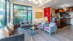 A modern hotel lobby with a seating area, a reception desk, and large windows offering a view of the outdoors. - The Living Hotel SamutPrakan (Bang Bo)