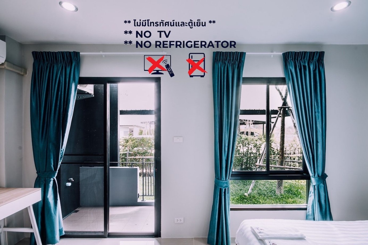 A hotel room with a bed, a desk, and a balcony. There are signs indicating no TV and no refrigerator.