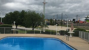 A swimming pool with a metal fence, a tall structure in the background, and a cloudy sky. - Twelve Oaks Inn (Branson)