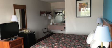 Een hotelkamer met een bed, een televisie, een dressoir, een bureau, een spiegel en een schilderij aan de muur.