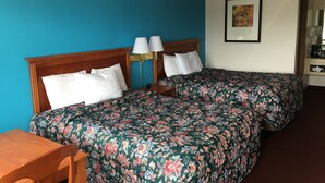 A hotel room with two single beds, a wooden desk, a chair, a nightstand with lamps, and a framed picture on the wall. - Twelve Oaks Inn (Branson)