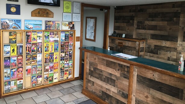 A reception area with a wooden counter, a television mounted on the wall, and a display of various movie posters. - Twelve Oaks Inn (Branson)