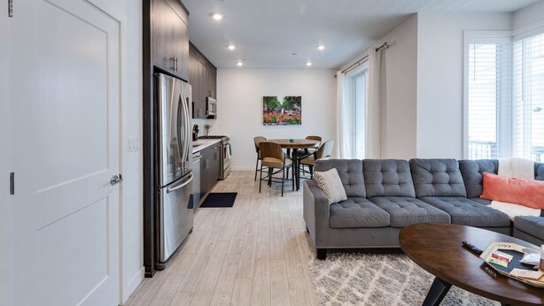 A modern kitchen with dark cabinets, a stainless steel refrigerator, and a dining area with a round table and chairs.