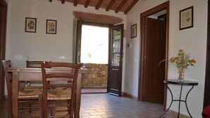 Un espace repas avec une table et des chaises en bois, un mur en pierre et une porte donnant sur l’extérieur.