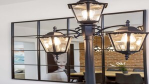 Ein modernes Interieur mit einer schwarzen Metalllüster, einem großen Spiegel, der einen Essbereich reflektiert, und einer Ziegelwand.