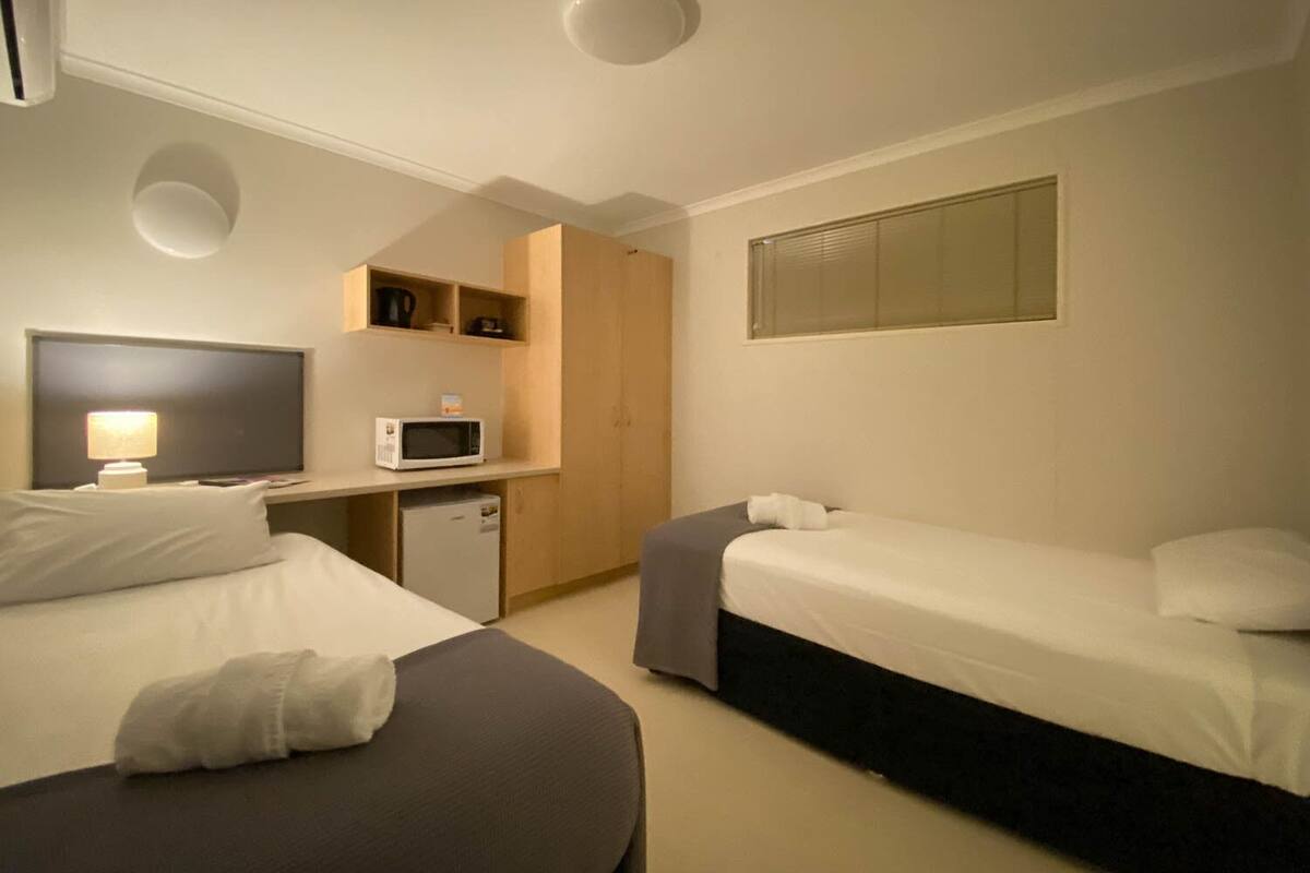 A hotel room with two beds, a TV, a microwave, and a small kitchenette.