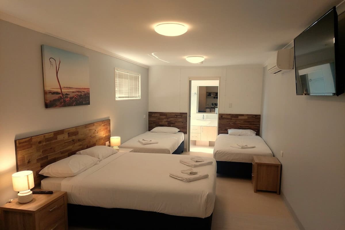 A hotel room with two beds, a TV, a painting, and a bathroom visible through an open door.