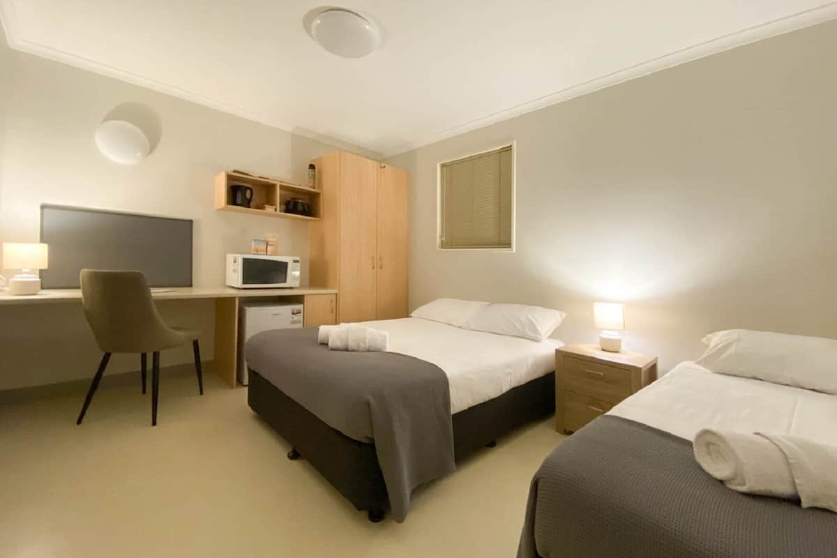 A hotel room with two beds, a desk, a chair, a microwave, and a wardrobe.