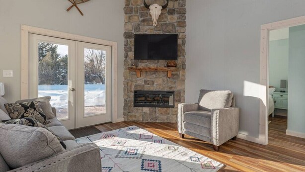 Una sala de estar acogedora con chimenea de piedra, un sillón cómodo y un ventanal con vistas a un paisaje nevado.