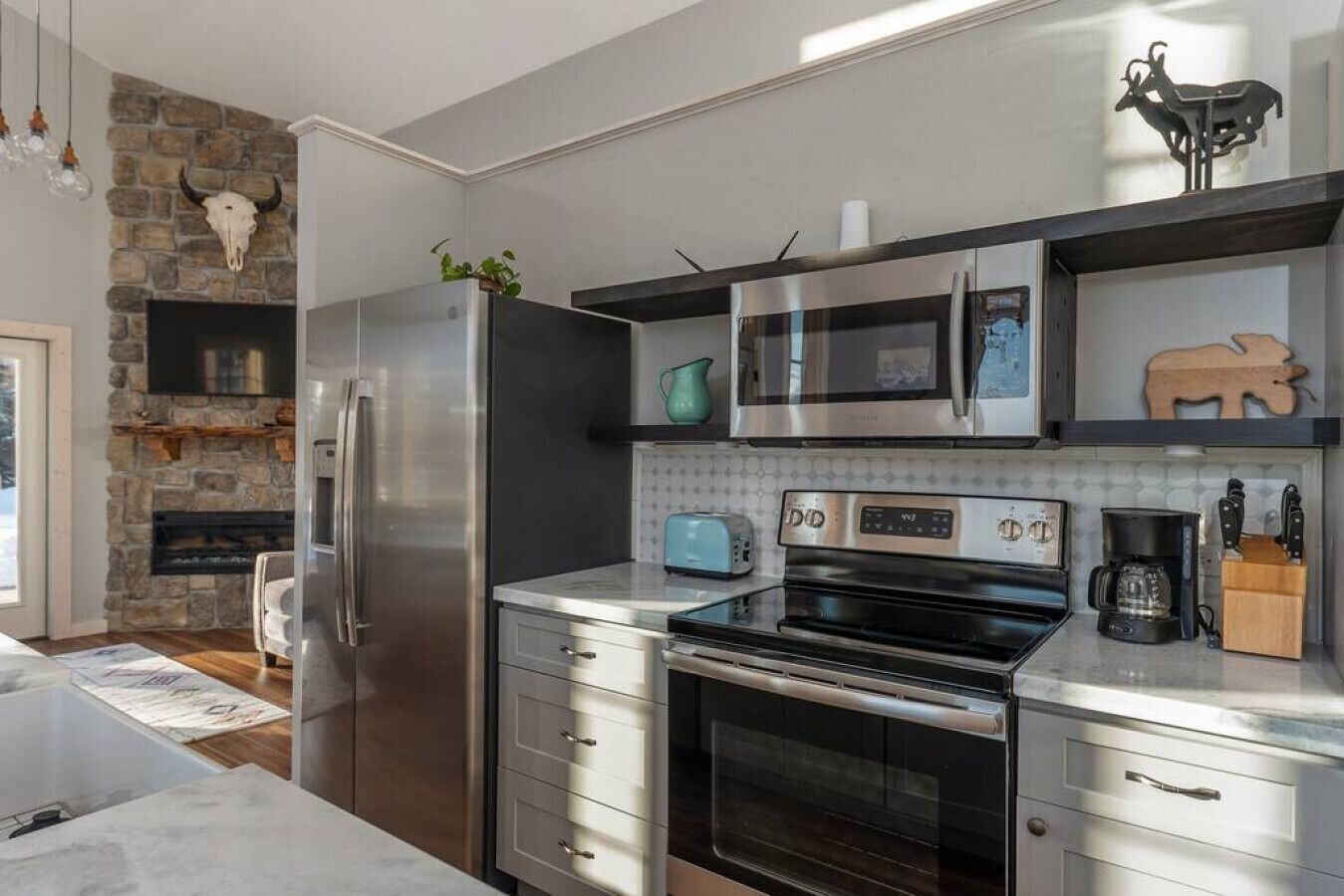 A modern kitchen with stainless steel appliances, a stone fireplace, and a wooden cow decoration.