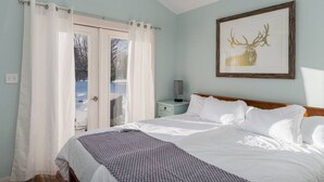 Un dormitorio con cama, cortinas blancas, una mesita de noche, una lámpara y un cuadro con una imagen de un ciervo en la pared.