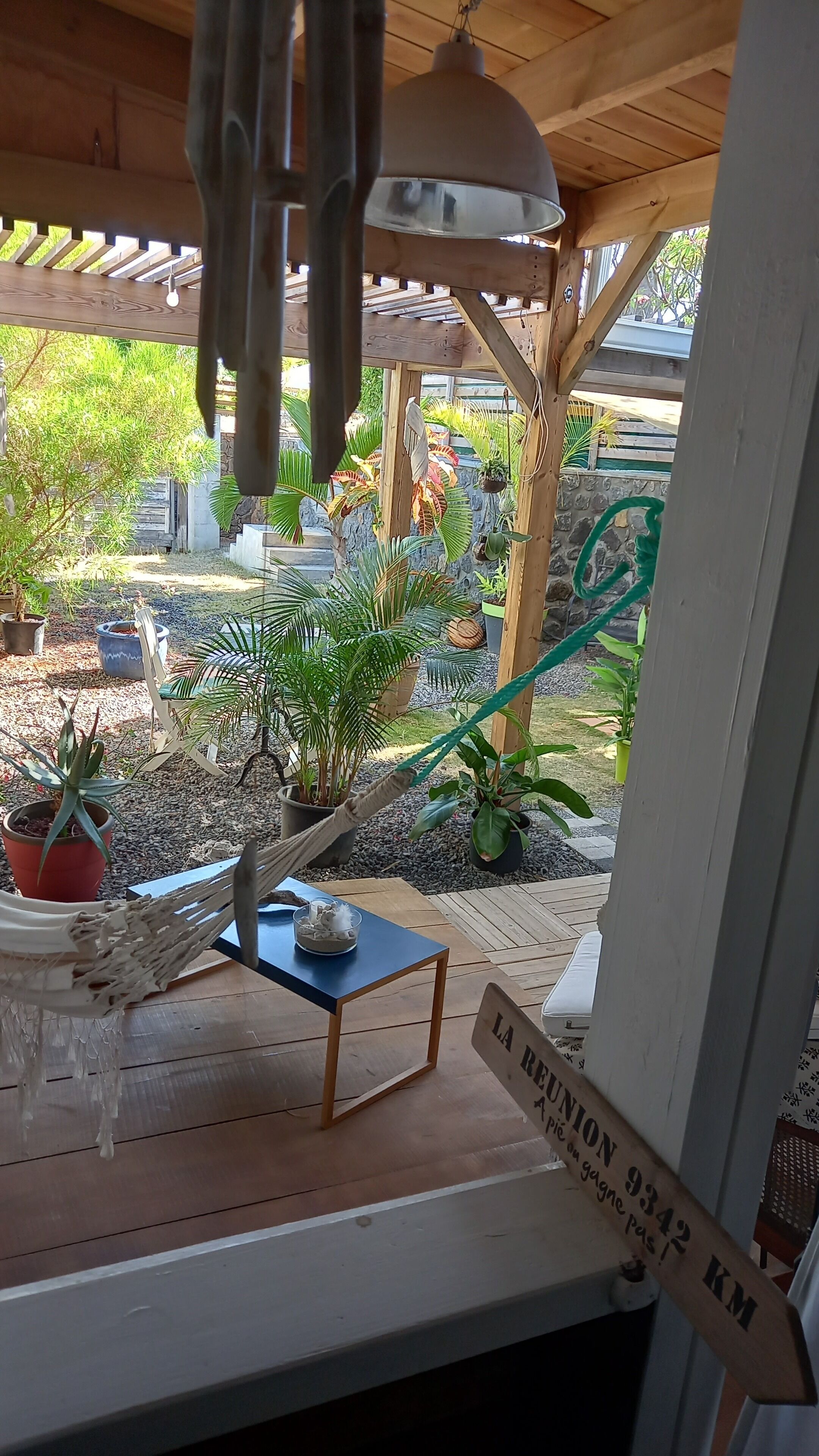 A covered outdoor area with a hammock, a small table, and various potted plants.