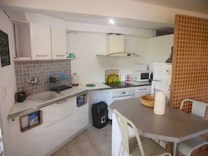 Une cuisine compacte avec des meubles blancs, un pare-feu en carrelage, un four à micro-ondes, une bouilloire et une petite table à manger avec des chaises.