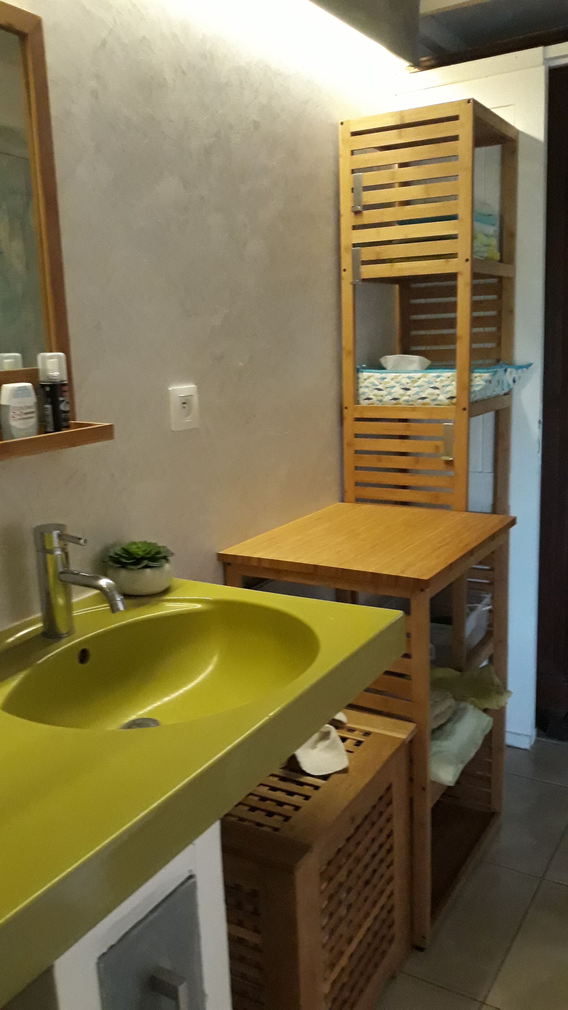 Un baño con un lavamanos verde, estantes de madera y un espejo.