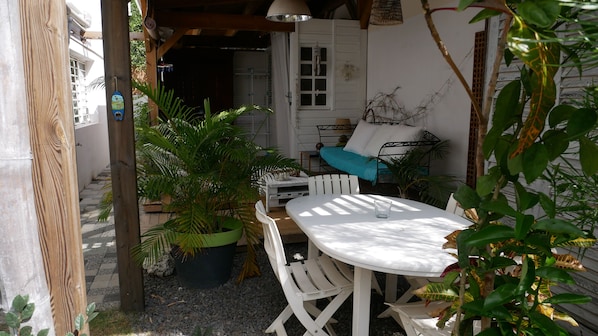 Une terrasse extérieure avec une table et des chaises blanches, entourée de plantes en pot et d  ’une pergola en bois.