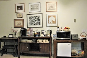 A kitchen with a microwave, toaster, and refrigerator. There are framed pictures on the wall and a coffee maker on the counter.