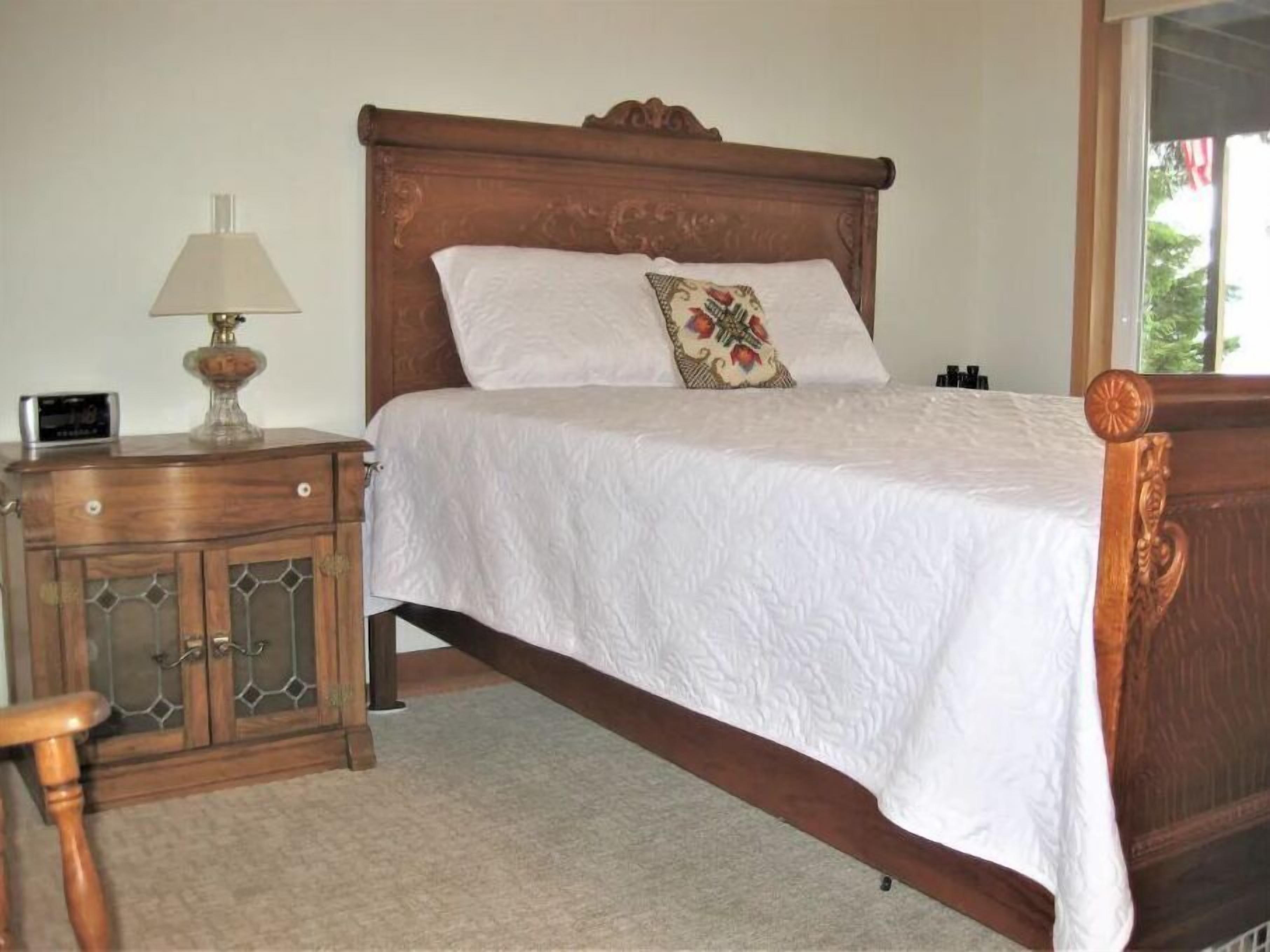 A bedroom with a wooden bed, a nightstand with a lamp, and a small cabinet.