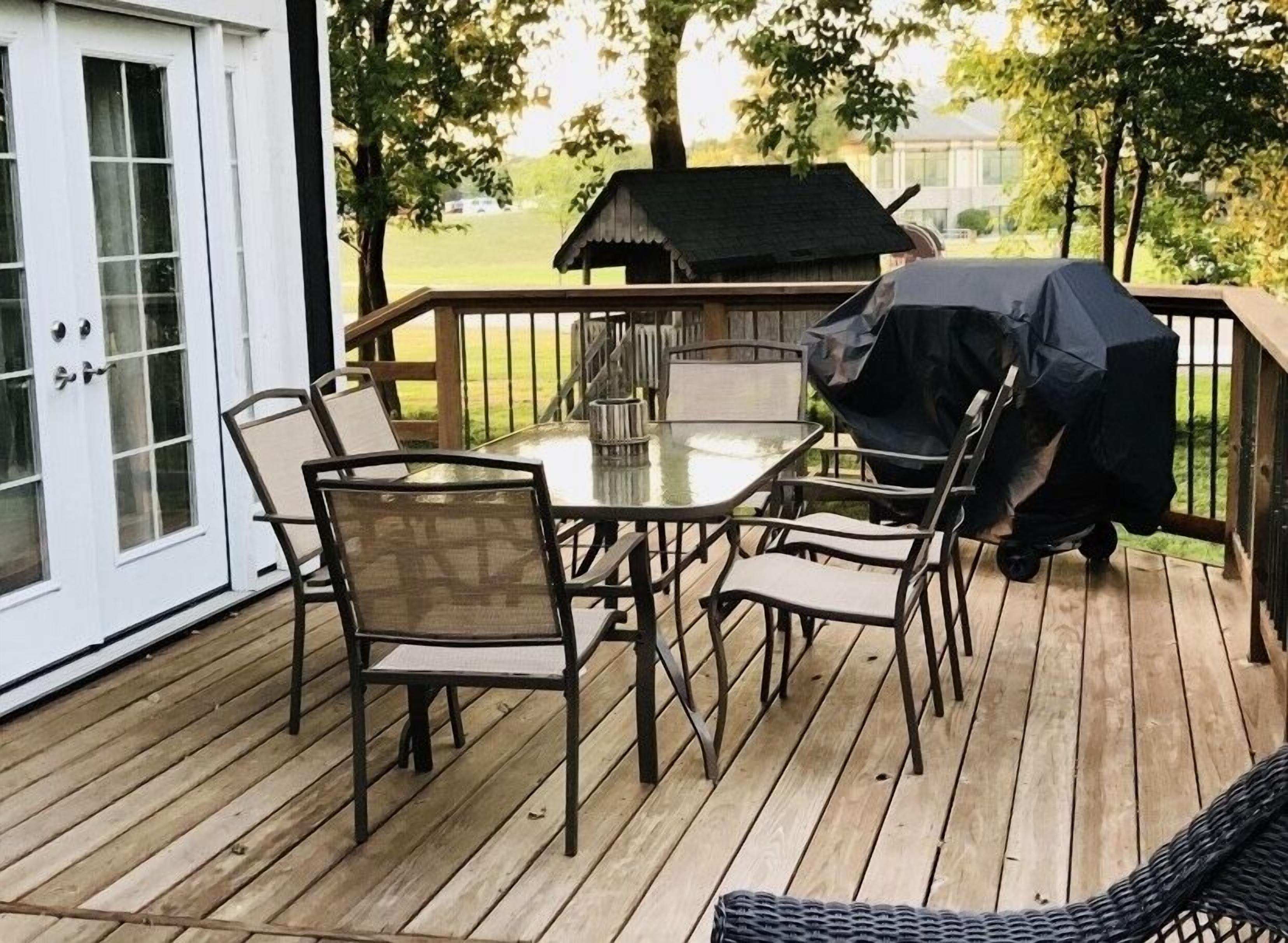 A wooden deck with a glass-top table and chairs, a barbecue grill, and a covered outdoor area.