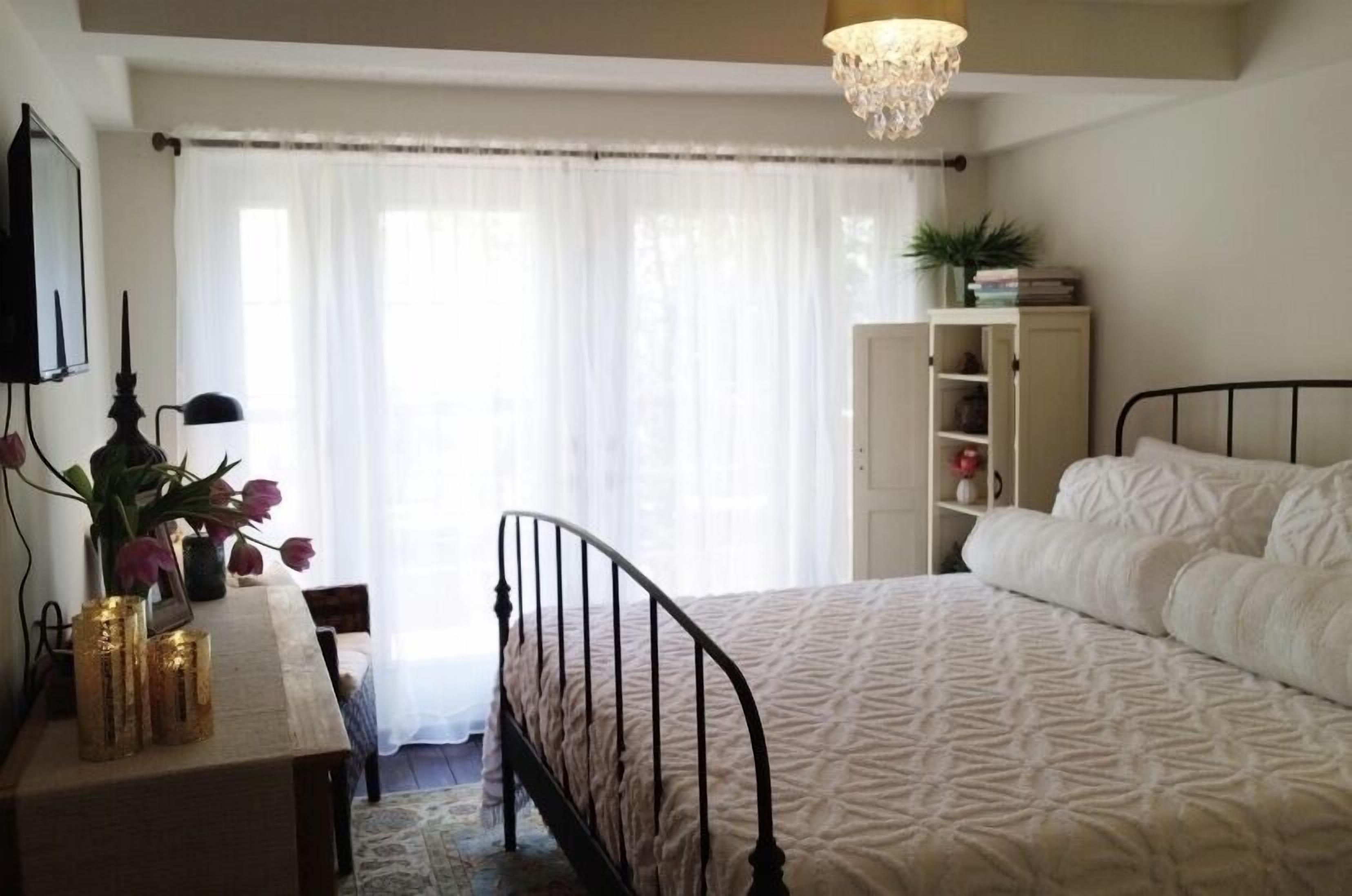 A bedroom with a bed, a desk with a lamp, a bookshelf, and a chandelier.