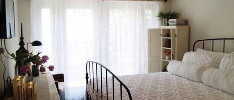 A bedroom with a bed, a desk with a lamp, a bookshelf, and a chandelier.