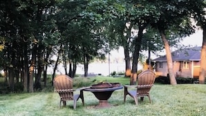 Een terras met een tafel en twee stoelen, omringd door bomen en een gazon.
