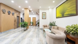 A hotel lobby with a marble floor, beige sofas, potted plants, a staircase, and wall clocks. - Winston Hotel Riverside (Ho Chi Minh City)