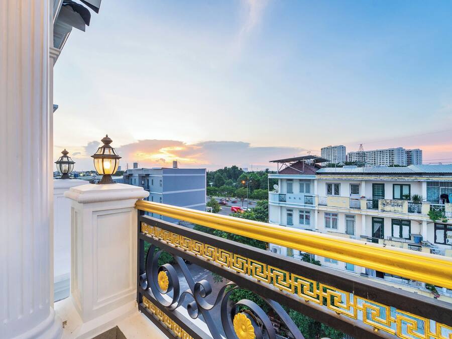 Un balcón con barandilla, vistas a edificios y una puesta de sol al fondo.