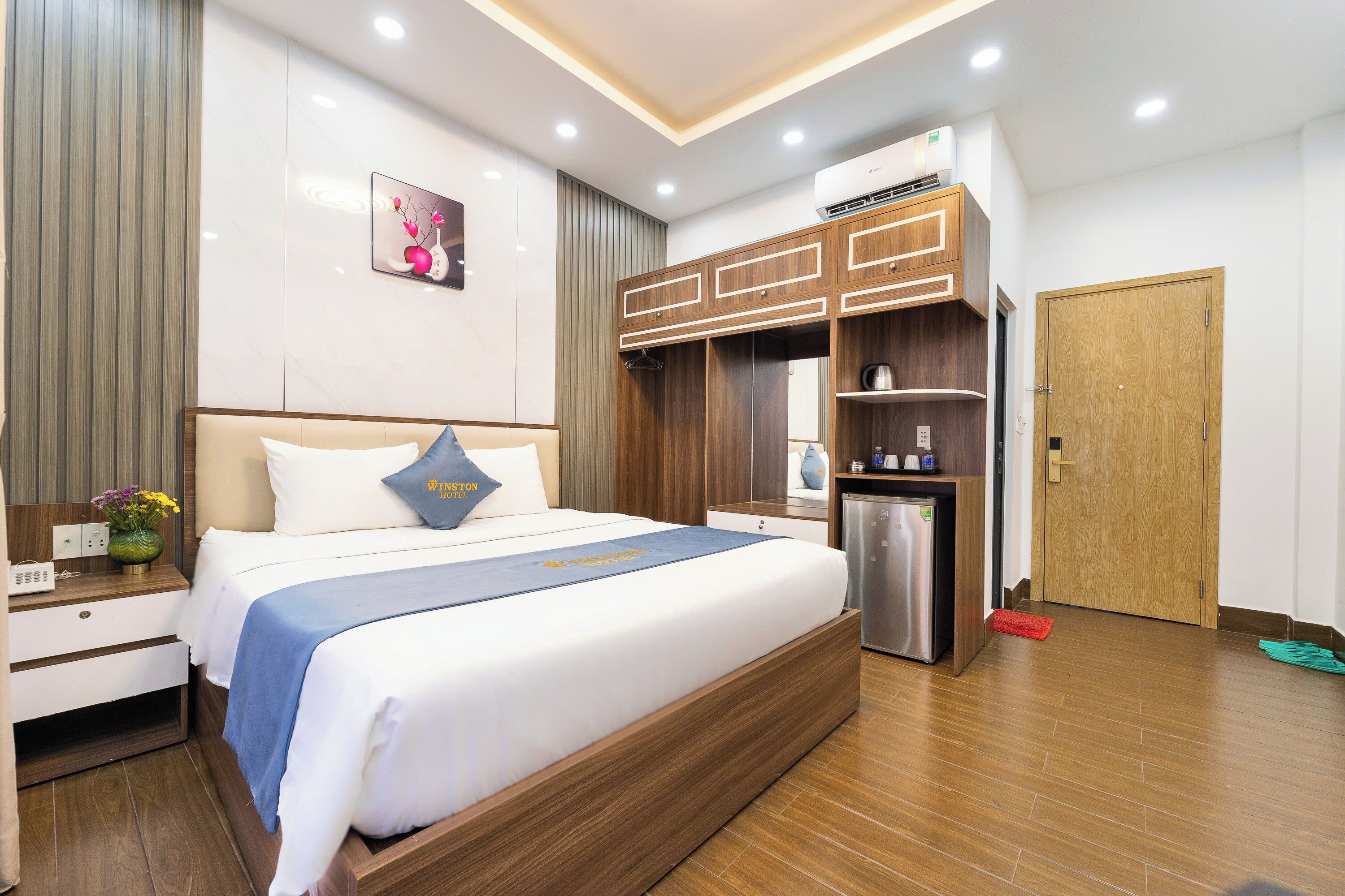A hotel room with a large bed, a wardrobe, a desk, and a small kitchenette.