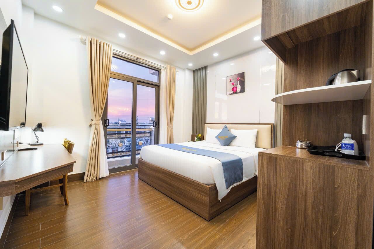 A hotel room with a bed, a desk, a TV, a window with curtains, and a city view.