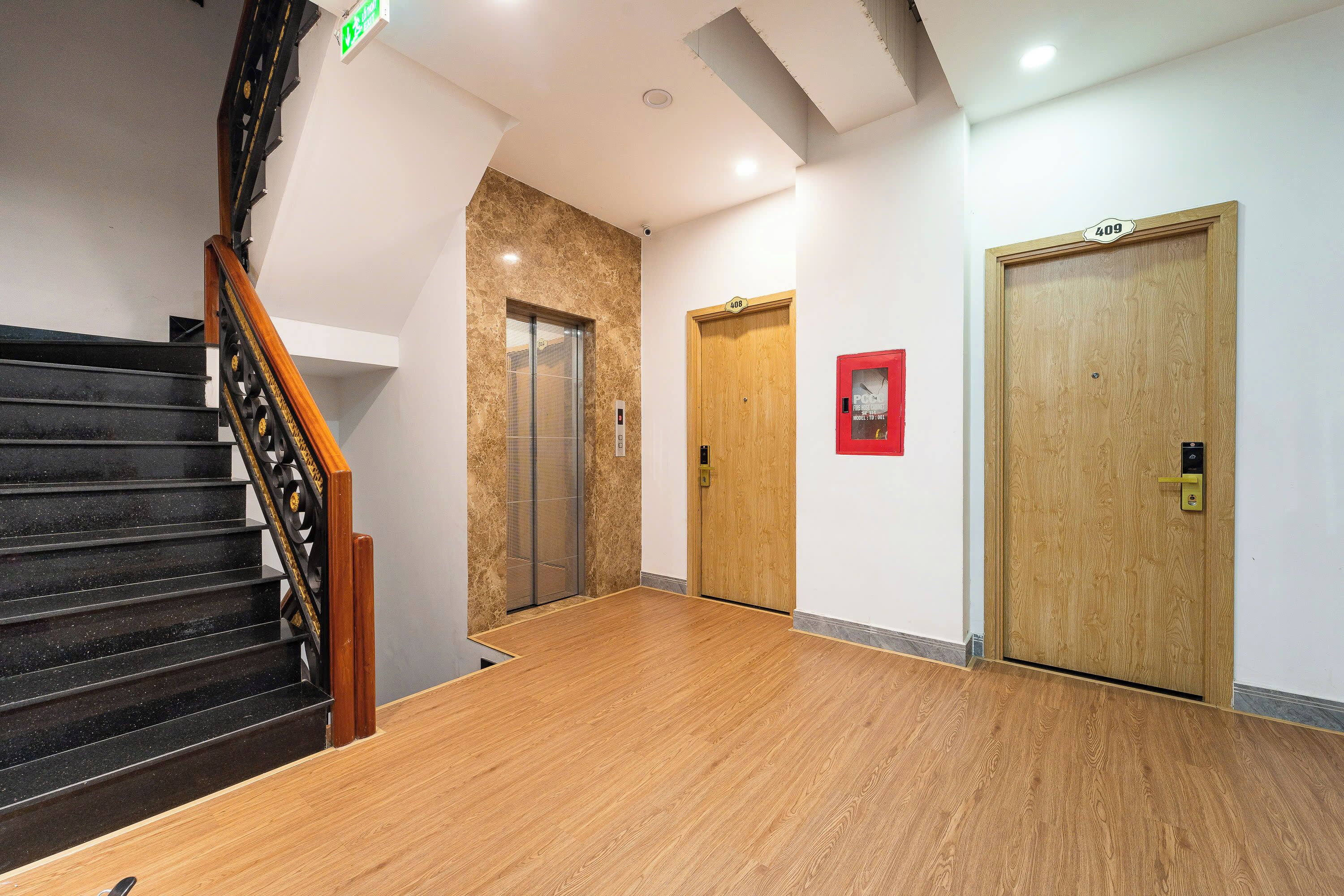 A hotel lobby with a wooden staircase, a marble wall, an elevator, and two wooden doors.