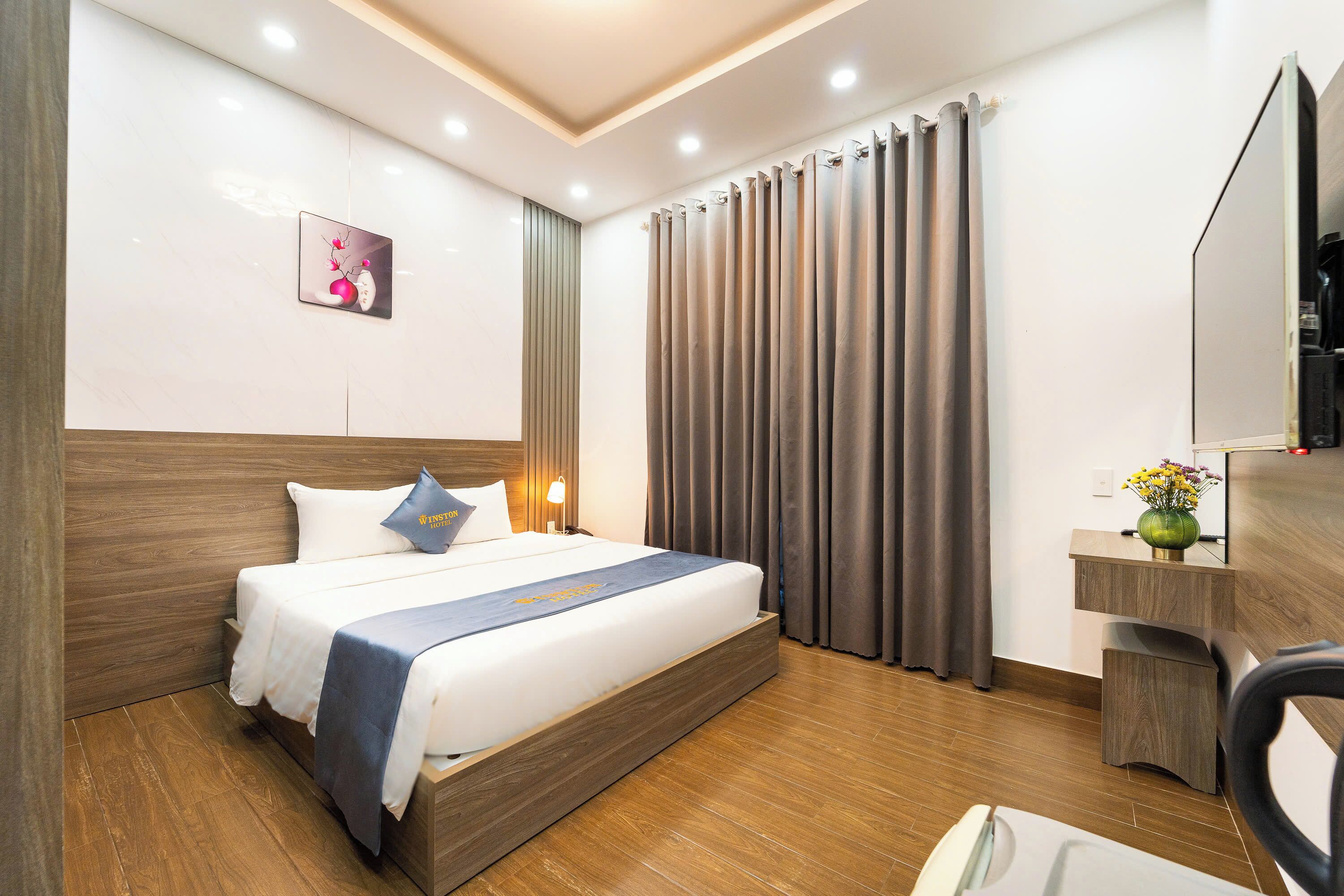 A hotel room with a bed, a desk, a chair, a mirror, and a picture on the wall.