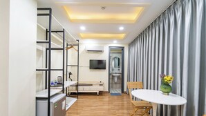 A modern hotel room with a wooden floor, a white table with chairs, a TV, a bathroom with a shower, and a curtain-covered window. - Winston Hotel Riverside (Ho Chi Minh City)